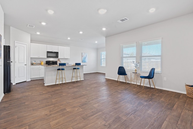 kitchen featuring dark wood-style flooring, visible vents, white cabinetry, black appliances, and a kitchen bar