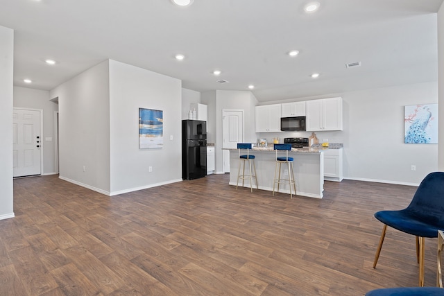 kitchen featuring a center island with sink, light stone counters, black appliances, white cabinets, and a kitchen bar