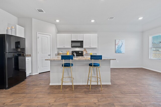 kitchen with white cabinetry, light stone counters, black appliances, a center island with sink, and dark hardwood / wood-style flooring