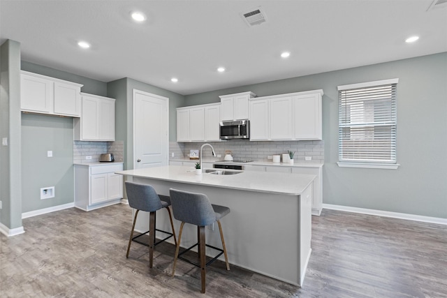 kitchen featuring white cabinetry, wood-type flooring, sink, and a center island with sink