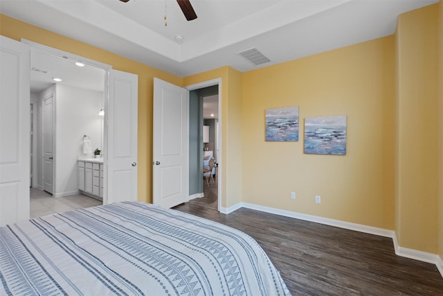 bedroom with ensuite bath, a raised ceiling, ceiling fan, and hardwood / wood-style flooring