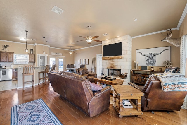 living room with ceiling fan, ornamental molding, wood-type flooring, and a stone fireplace