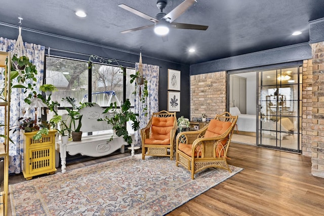 sitting room with hardwood / wood-style flooring, ceiling fan, and brick wall