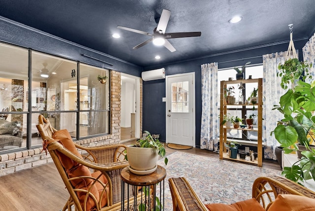 sitting room with crown molding, wood-type flooring, a textured ceiling, a wall unit AC, and ceiling fan