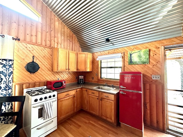 kitchen with vaulted ceiling, wooden walls, sink, fridge, and gas range gas stove