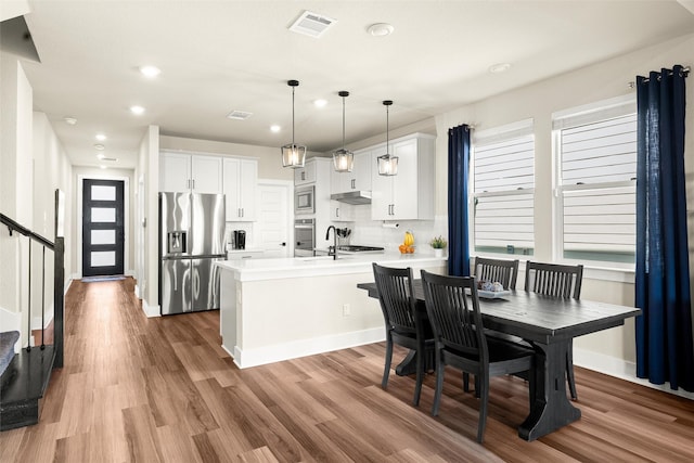 kitchen featuring appliances with stainless steel finishes, pendant lighting, wood-type flooring, white cabinets, and decorative backsplash