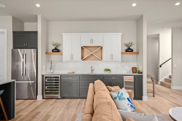 bar with wine cooler, gray cabinets, high quality fridge, and light wood-type flooring