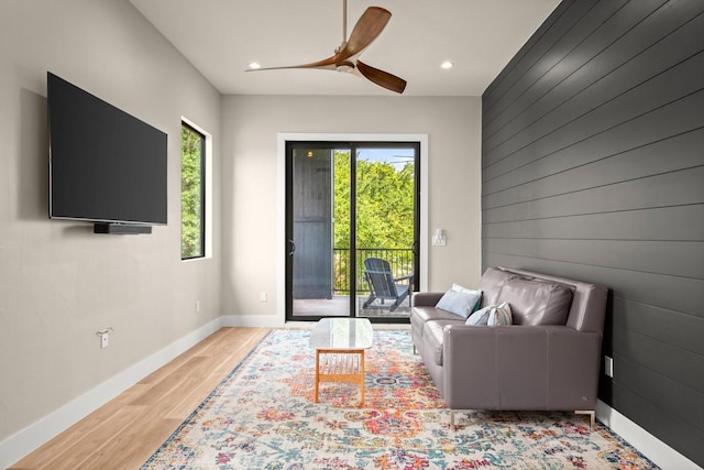 living room with light hardwood / wood-style flooring, ceiling fan, and wood walls