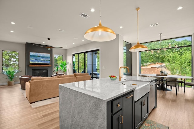 kitchen featuring light stone countertops, an island with sink, hanging light fixtures, and light wood-type flooring