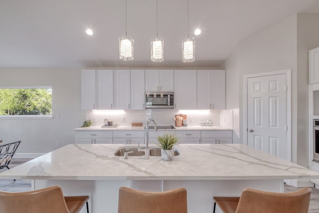 kitchen with stainless steel appliances, a kitchen island with sink, sink, and white cabinets