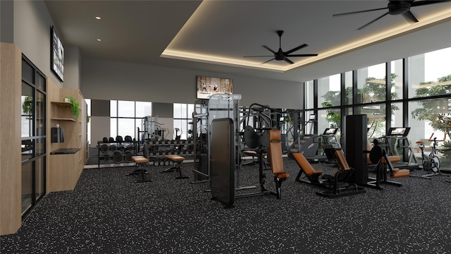 gym featuring a raised ceiling, floor to ceiling windows, and ceiling fan