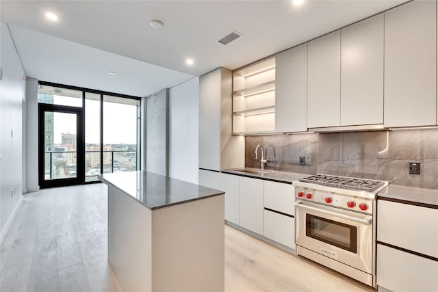 kitchen featuring tasteful backsplash, a wall of windows, a center island, designer stove, and light hardwood / wood-style flooring