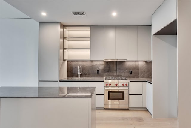 kitchen with sink, tasteful backsplash, white cabinetry, premium range, and light hardwood / wood-style floors