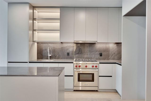 kitchen featuring tasteful backsplash, sink, luxury stove, and white cabinetry