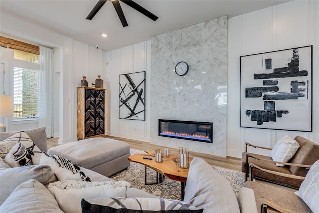 living room featuring ceiling fan, a premium fireplace, and light hardwood / wood-style floors