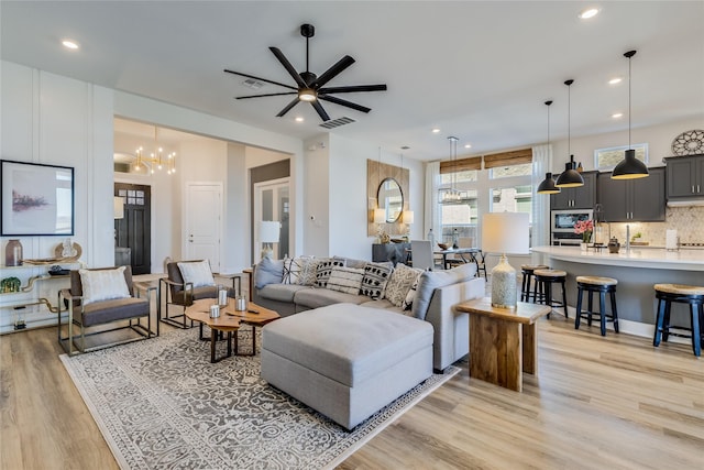 living room featuring ceiling fan with notable chandelier and light wood-type flooring