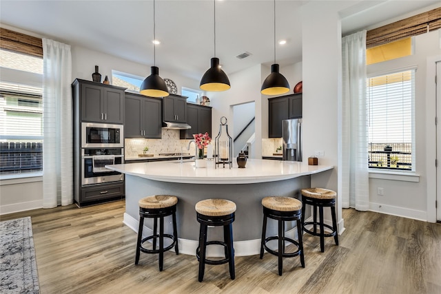 kitchen featuring appliances with stainless steel finishes, a kitchen bar, wood-type flooring, and hanging light fixtures