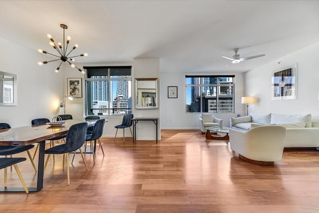 dining space with ceiling fan with notable chandelier and light wood-type flooring