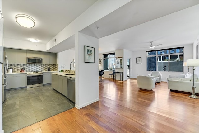 kitchen featuring sink, ceiling fan, appliances with stainless steel finishes, tasteful backsplash, and light wood-type flooring