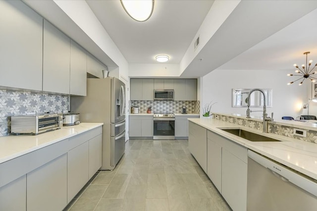 kitchen featuring tasteful backsplash, sink, gray cabinetry, a chandelier, and stainless steel appliances