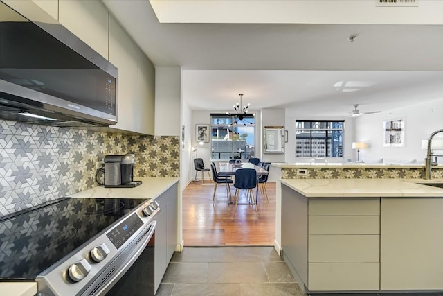 kitchen with ceiling fan with notable chandelier, sink, backsplash, light stone counters, and stainless steel appliances