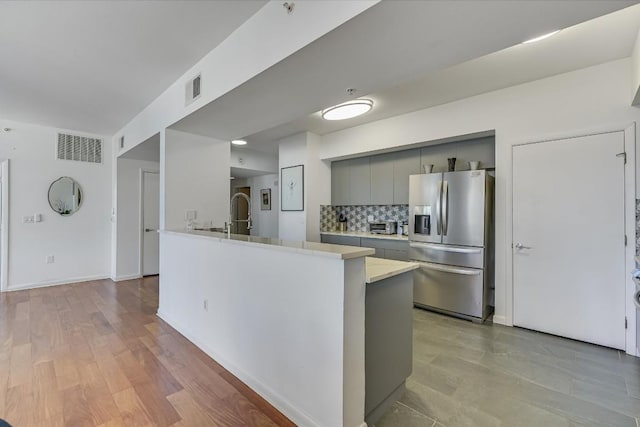 kitchen with stainless steel fridge, gray cabinets, backsplash, kitchen peninsula, and light wood-type flooring