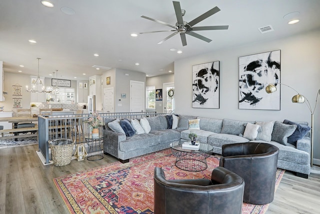 living room with ceiling fan with notable chandelier and light wood-type flooring