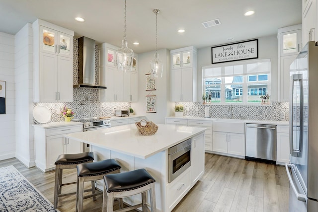 kitchen with white cabinetry, a kitchen breakfast bar, a kitchen island, stainless steel appliances, and wall chimney range hood