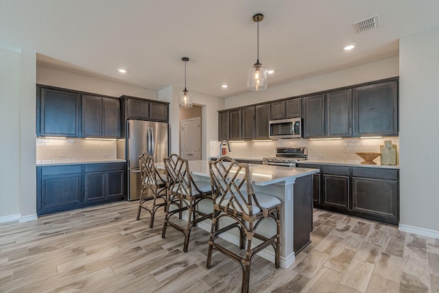 kitchen with an island with sink, a kitchen bar, hanging light fixtures, stainless steel appliances, and light hardwood / wood-style flooring