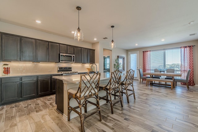 kitchen featuring pendant lighting, a breakfast bar area, a kitchen island with sink, light hardwood / wood-style floors, and stainless steel appliances