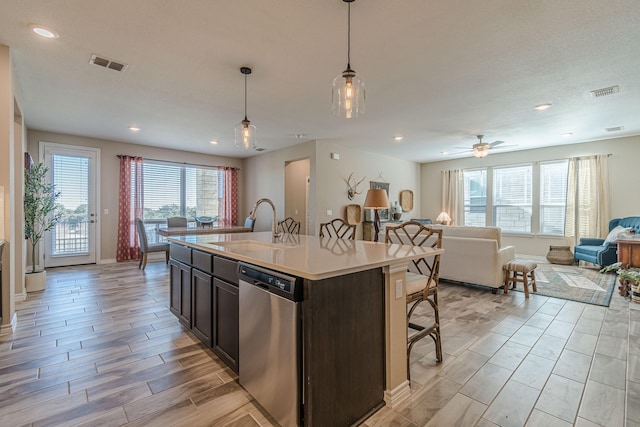 kitchen featuring pendant lighting, dishwasher, sink, dark brown cabinets, and a center island with sink