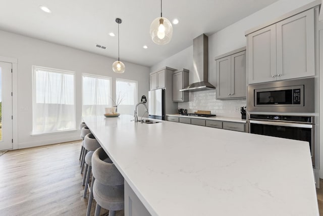 kitchen with hanging light fixtures, appliances with stainless steel finishes, gray cabinets, wall chimney range hood, and backsplash