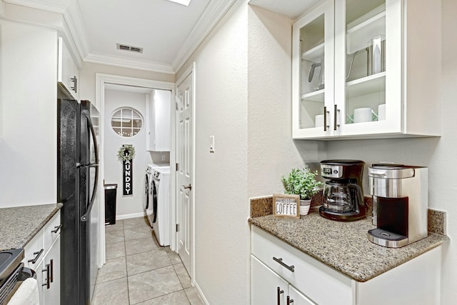 kitchen featuring washing machine and clothes dryer, black fridge, crown molding, light tile patterned floors, and white cabinets