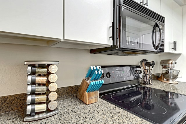 interior details with light stone counters, white cabinets, and black appliances