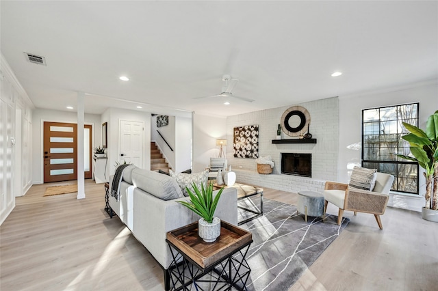 living room with ceiling fan, light wood-type flooring, crown molding, and a fireplace