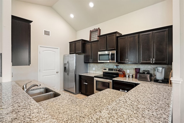 kitchen with sink, appliances with stainless steel finishes, high vaulted ceiling, tasteful backsplash, and light stone countertops