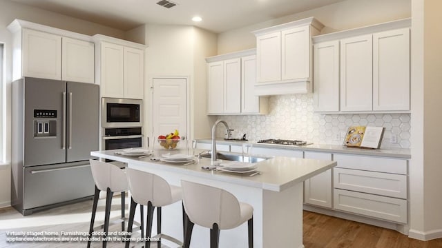 kitchen with stainless steel appliances, a kitchen island with sink, decorative backsplash, and white cabinets