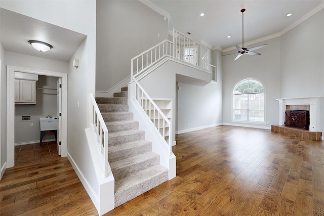 staircase featuring sink, wood-type flooring, ceiling fan, a fireplace, and a high ceiling