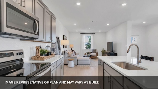 kitchen featuring sink, appliances with stainless steel finishes, gray cabinets, light hardwood / wood-style floors, and backsplash