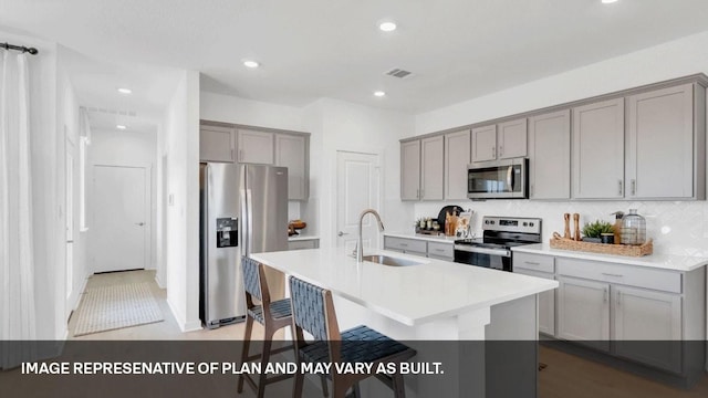 kitchen featuring sink, gray cabinets, stainless steel appliances, and a center island with sink