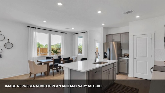 kitchen featuring sink, light hardwood / wood-style flooring, gray cabinets, appliances with stainless steel finishes, and an island with sink