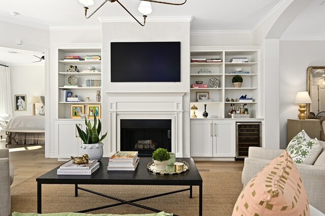 living room featuring built in features, ornamental molding, wine cooler, and light wood-type flooring