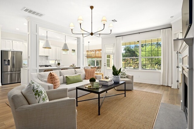 living room with an inviting chandelier, crown molding, and light hardwood / wood-style floors