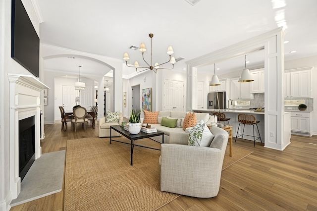 living room with crown molding, sink, hardwood / wood-style floors, and a notable chandelier