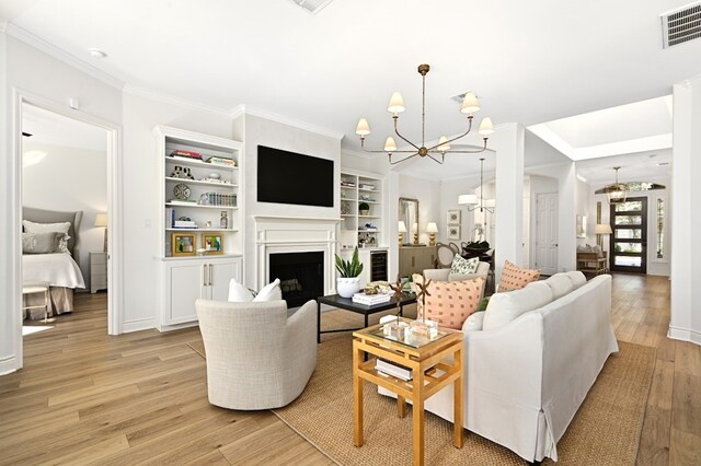 living room with ornamental molding, light hardwood / wood-style flooring, an inviting chandelier, and built in shelves