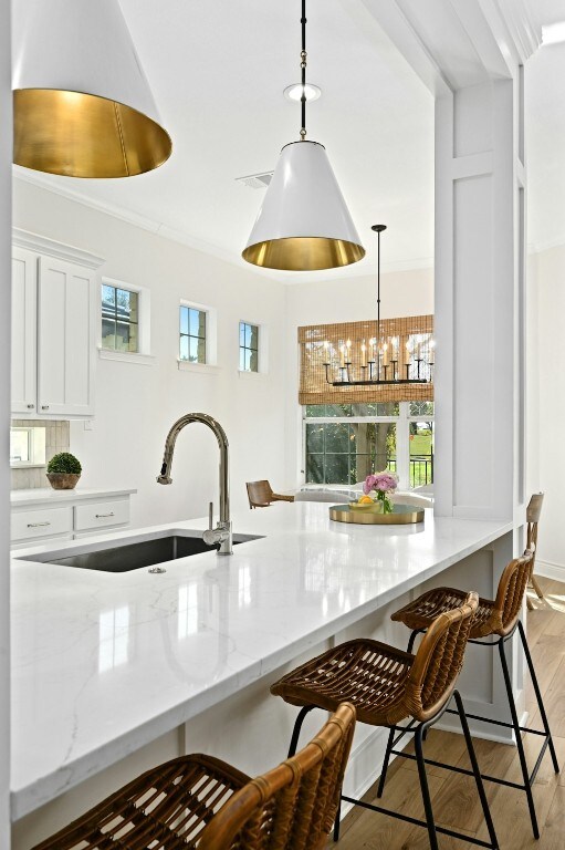 kitchen with sink, a breakfast bar area, white cabinets, decorative light fixtures, and light wood-type flooring