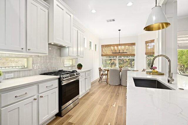 kitchen with sink, stainless steel gas range, white cabinetry, backsplash, and decorative light fixtures