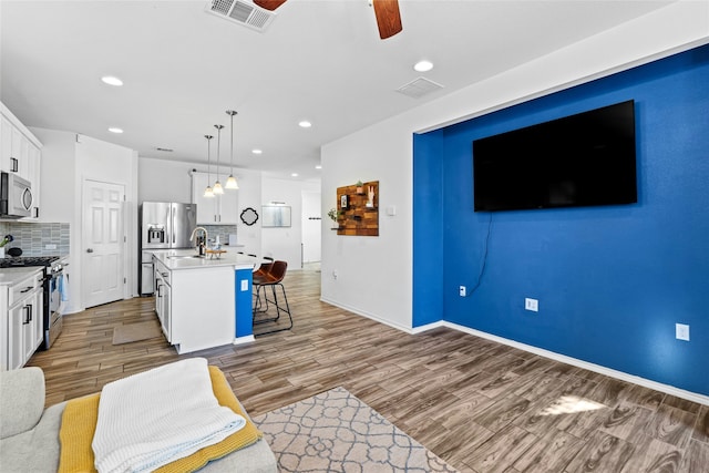 kitchen featuring pendant lighting, white cabinetry, backsplash, stainless steel appliances, and a center island with sink