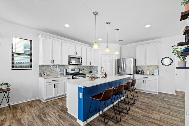 kitchen with a kitchen bar, white cabinetry, decorative light fixtures, stainless steel appliances, and a kitchen island with sink