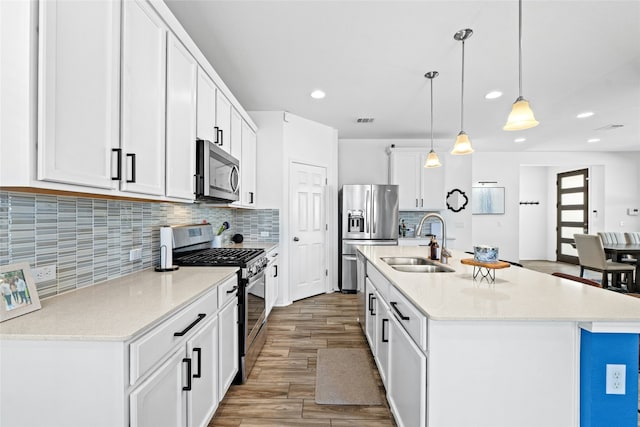 kitchen with pendant lighting, sink, appliances with stainless steel finishes, white cabinetry, and an island with sink